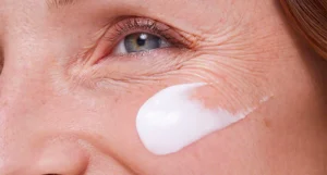 Close-up of a person applying white cream on their cheek.